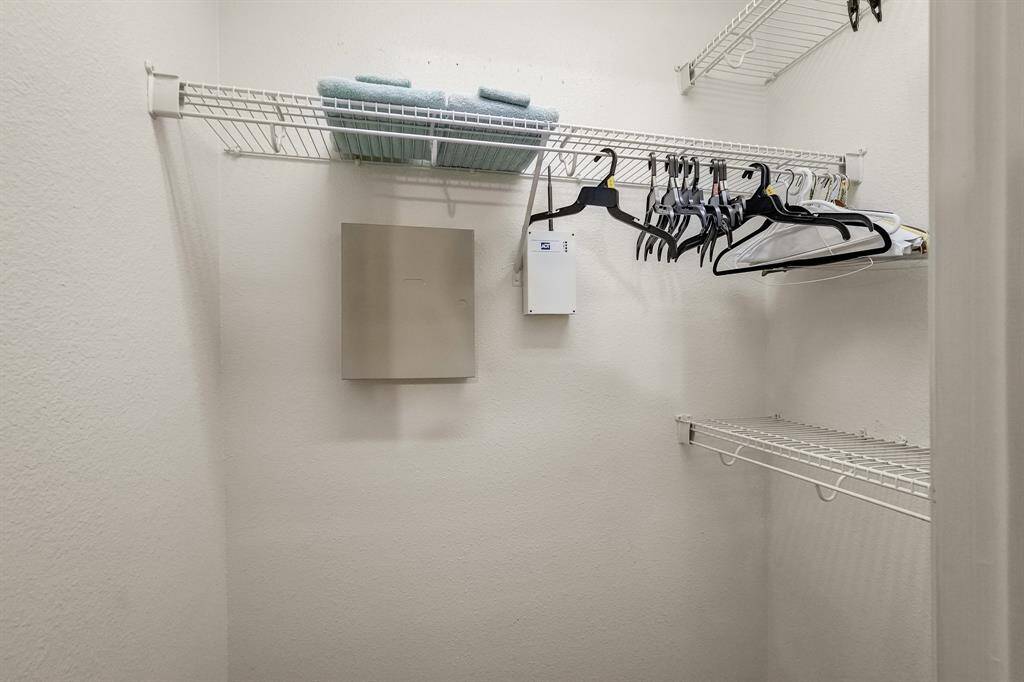 This photo shows a small walk-in closet with white wire shelving, hangers, and neatly folded towels, offering practical storage space.