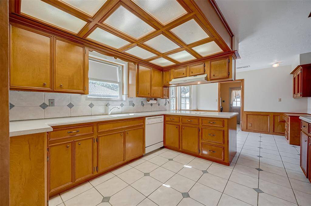 The kitchen boasts double Corian sinks with a window overlooking the driveway and side yard. To the right of the sink, you'll find a convenient Kennore dishwasher. The tile backsplash design is mirrored in the tile flooring, creating a cohesive and harmonious look throughout the space.