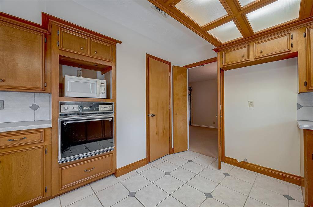 The kitchen includes a microwave and electric oven, both functional but dated. Prospective buyers may opt to upgrade to double ovens, convection ovens, or a combined oven and convection microwave unit to better align with their cooking preferences. A lower drawer provides convenient storage for baking sheets and casserole dishes, maximizing kitchen efficiency and organization. A door on the right opens to a lighted, walk-in pantry with ample storage.