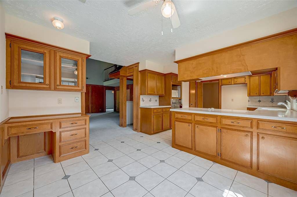 The kitchen seamlessly flows into a breakfast area, which features a built-in planning desk with upper glass display cabinets. This space is perfect for managing household bills and tasks. Some families are repurposing the desk area as a coffee bar by removing the desk drawer and installing a beverage refrigerator below, creating a convenient spot for coffee and drinks.