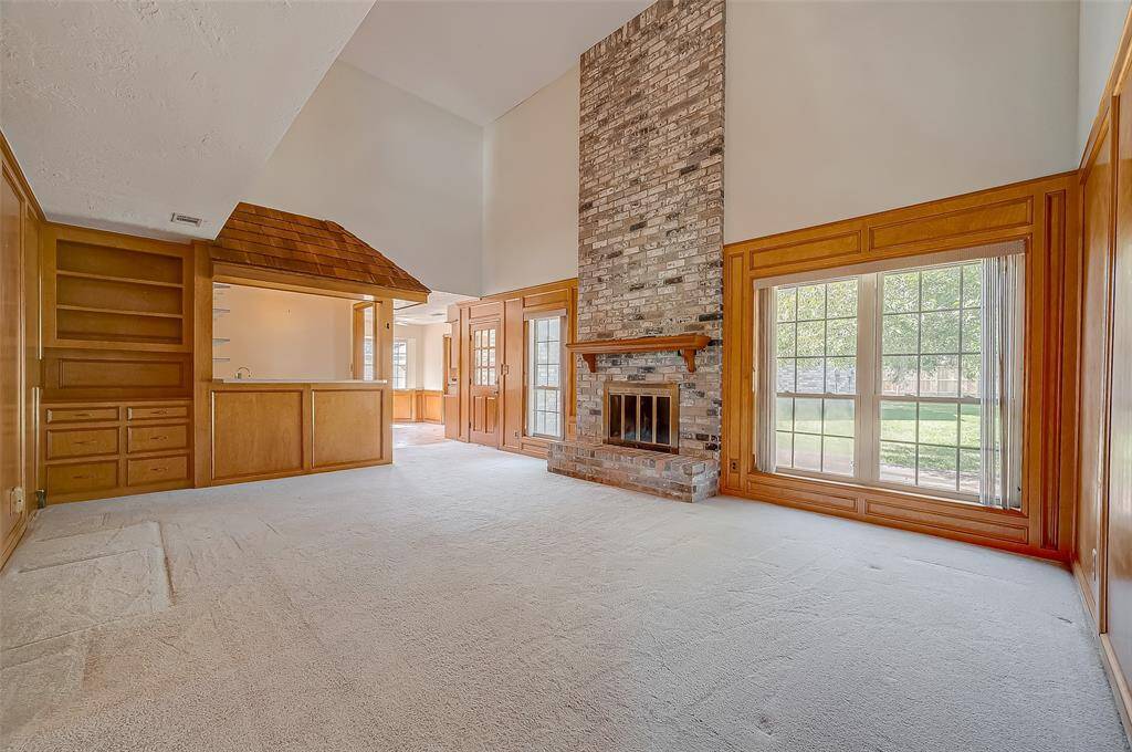 The breakfast area flows seamlessly into the family room, featuring a soaring 2-story brick fireplace that serves as a striking focal point. Walls of windows overlook the backyard, filling the space with natural light. A built-in bookcase with 6-drawer cabinet below provides a perfect spot to display family treasures, while a walk-in wet bar enhances the room's entertainment potential.