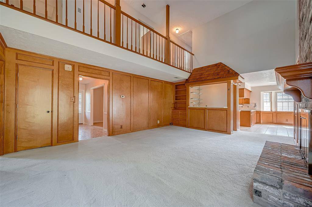 The family room, measuring 19.7 x 15.5, features warm honey-colored wood paneling and a soaring 2-story ceiling. A catwalk hallway on the second floor connects to the three secondary bedrooms and a shared bathroom. A door on the left opens to a deep coat closet with additional storage beneath the stairs.