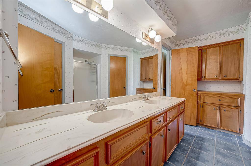 The owner's suite ensuite bath, measuring 12.6 x 6.10, offers a functional and practical layout. It features double sinks in a long cultured marble vanity with a wall-length mirror and overhead lighting. Along the far wall, there is a built-in storage cabinet for linens and a built-in clothes hamper, enhancing convenience and organization.