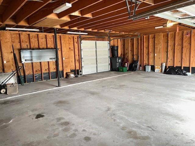 The interior of the garage showcases its practical design and functionality. The 8-ft roll-up rear bay door provides convenient pull-through access to the backyard, perfect for storing a boat or trailer. Overhead, there is 500 sqft of decked storage, accessed via heavy-duty disappearing stairs, ideal for keeping items organized and out of the way. The unfinished walls offer flexibility for customization or easy access for running additional utilities if needed.
