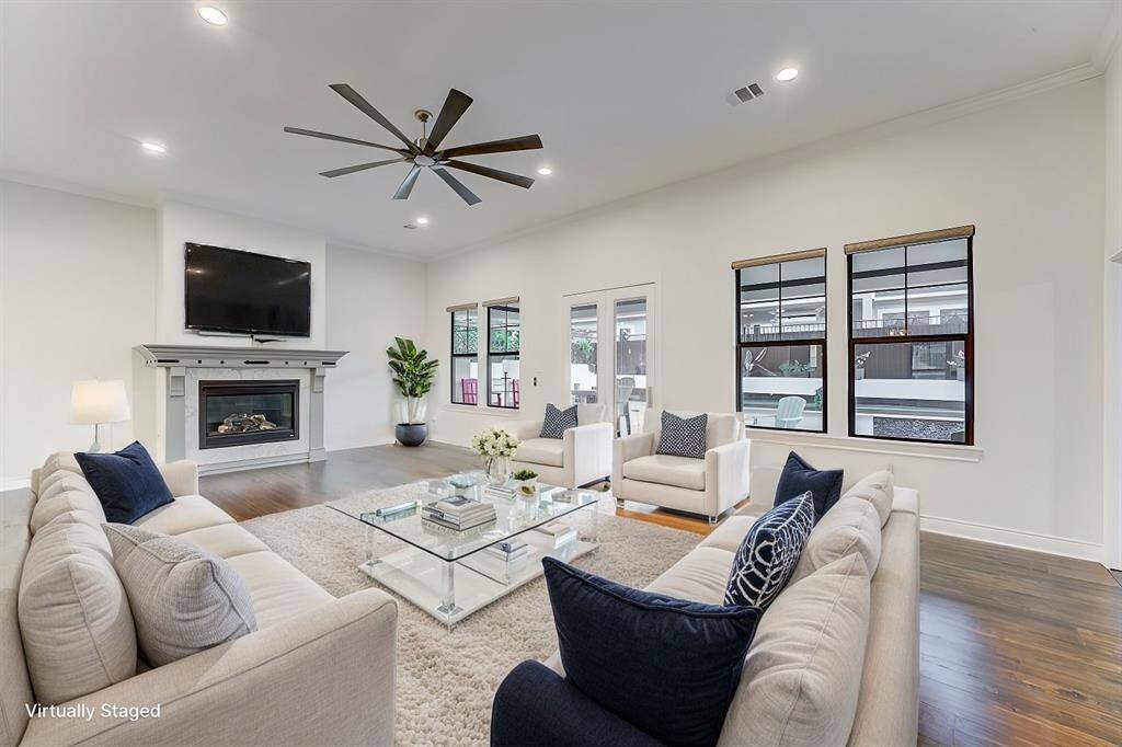 Virtually staged - This is a spacious, well-lit living room featuring a cozy fireplace and large windows with a view to the outside. There's also direct access to the back patio area through the French doors.