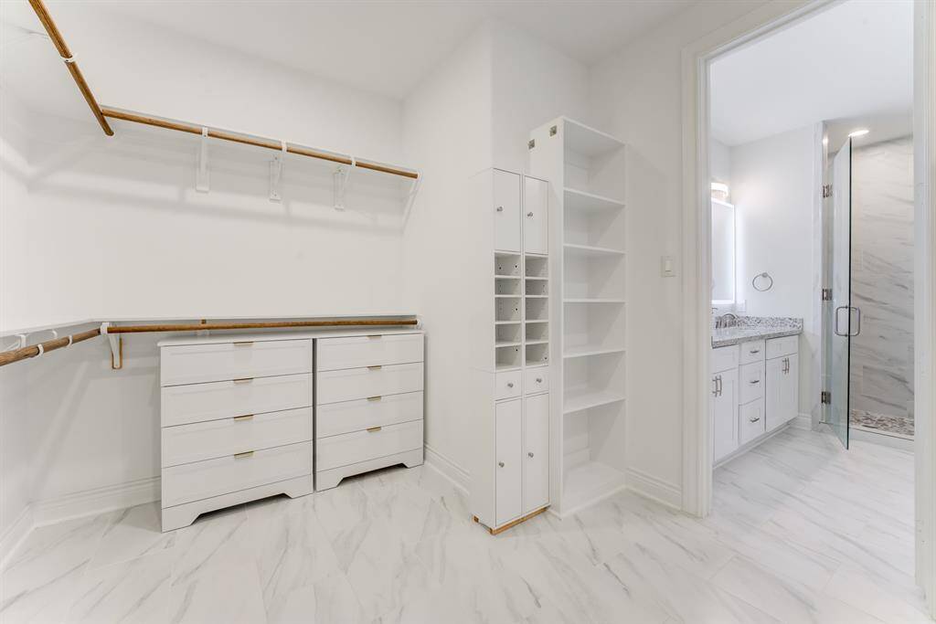 This is a well-organized dream closet with built-in white cabinetry, ample hanging space, and an adjacent modern bathroom.