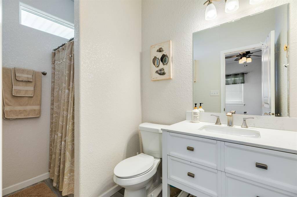 This 2nd story guest bathroom features a modern white vanity with dual sinks, a large mirror, and a shower with a patterned curtain. Neutral tones create a clean and inviting atmosphere.
