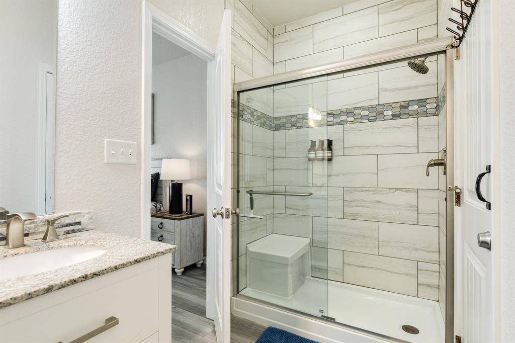 Modern primary bathroom with a glass-enclosed tiled shower featuring elegant tile work and a sleek vanity with a granite countertop.