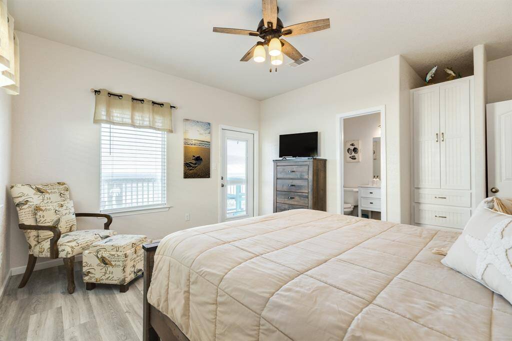 Bright bedroom with a neutral color palette, featuring a comfortable bed, elegant armchair, and ample storage. A ceiling fan adds comfort, while the window and glass door provide natural light and access to 2nd level deck.