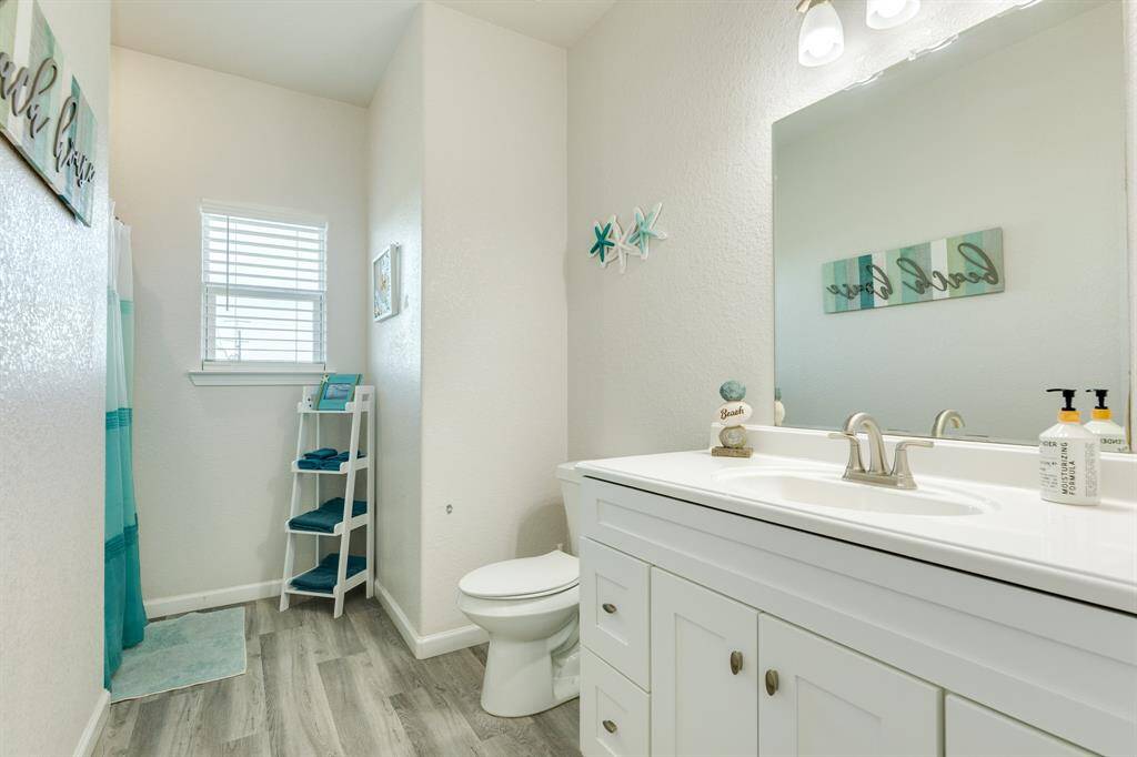This is a bright and modern 2nd story guest bath featuring a white vanity with a large mirror, coastal-themed decor, light wood flooring, and a window for natural light.