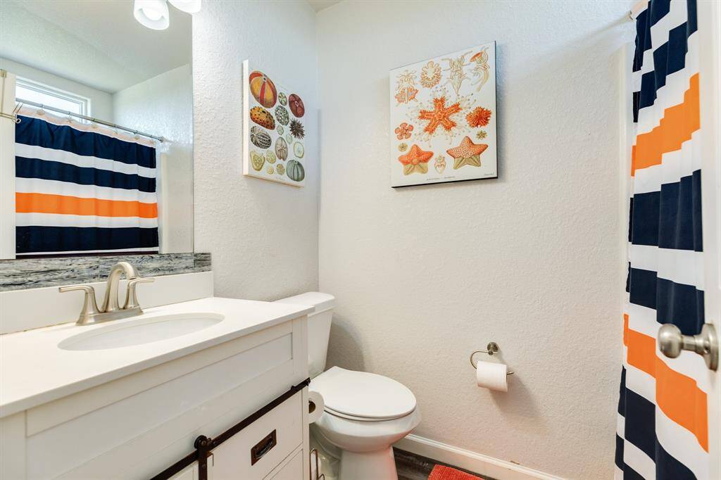 This 1st floor ensuite bath features a modern white vanity with a sleek faucet, a colorful shower curtain with bold stripes, and decorative wall art. It has a bright and clean look with a practical layout.