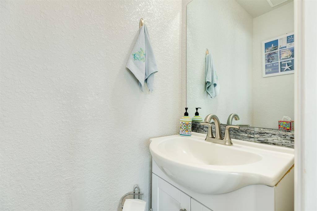 This 1st floor half bath features a vanity with a stylish faucet, large mirror, and white walls.