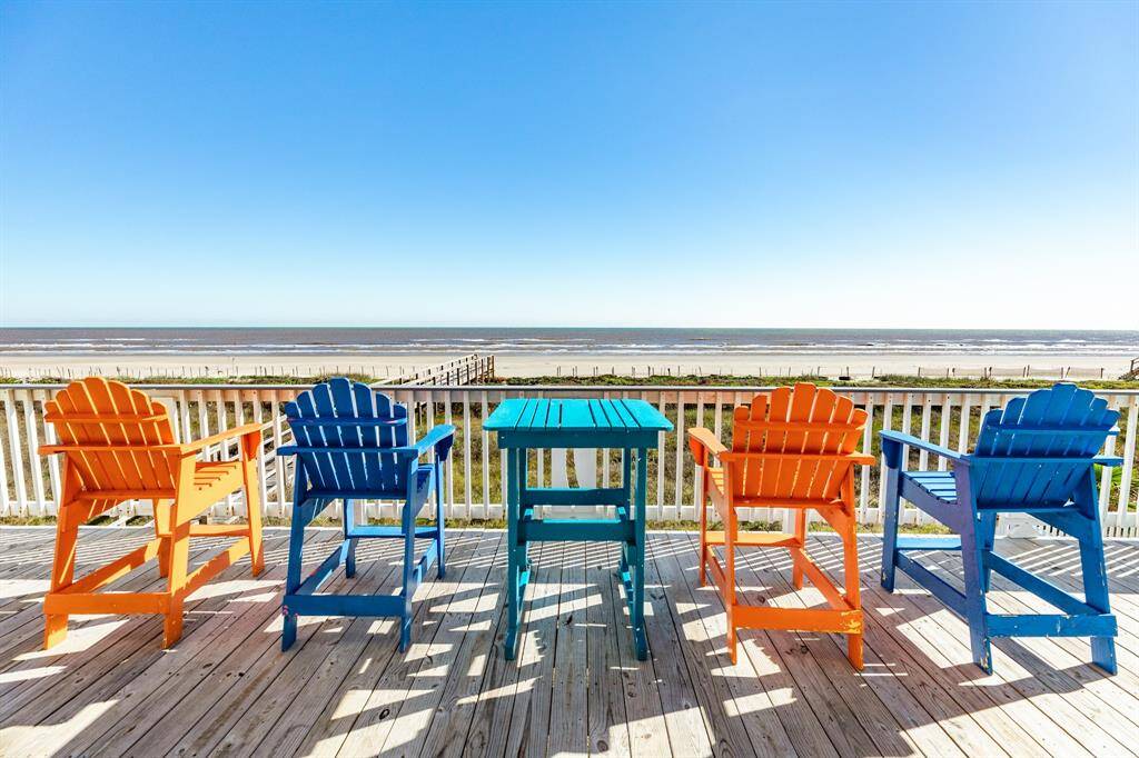 You gotta love a beachfront deck with vibrant orange and blue Adirondack chairs and  table, offering stunning views. Perfect for relaxing and enjoying the Texas gulf coast.