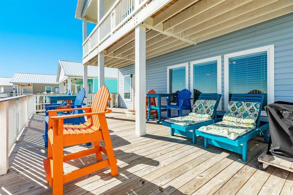 This photo showcases a spacious wooden deck with vibrant seating, perfect for relaxing or entertaining. The light blue siding and large windows add a cheerful touch, while the deck offers ample space and a sunny atmosphere and is partially covered.