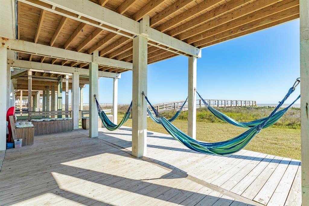 This photo shows a spacious, covered deck featuring hammocks and scenic views of a grassy area leading to a beachfront walkover, perfect for relaxation and enjoying outdoor living.