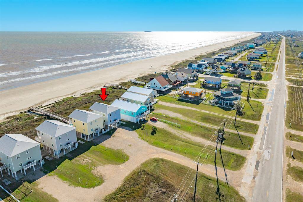 This aerial photo shows beachfront homes with direct access to a sandy beach. The highlighted property is close to the shoreline, offering stunning ocean views. The neighborhood features elevated houses, providing a serene coastal living experience.