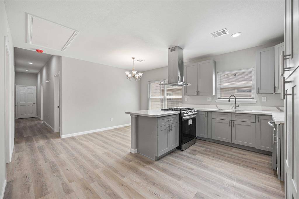 This photo showcases a bright, modern kitchen with gray cabinets, a central island, and stainless steel appliances. The open layout and light wood flooring create a spacious feel, extending into an adjacent dining area.