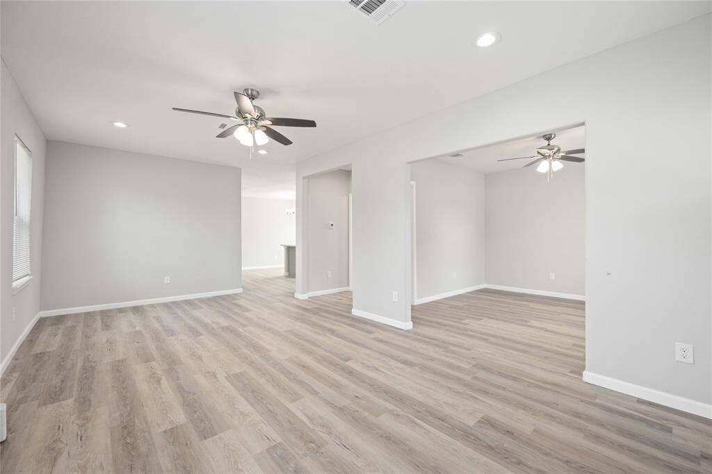 The photo showcases a modern, open-concept living space with light gray walls and wood-style flooring. It features ceiling fans and recessed lighting, offering a bright and airy atmosphere.