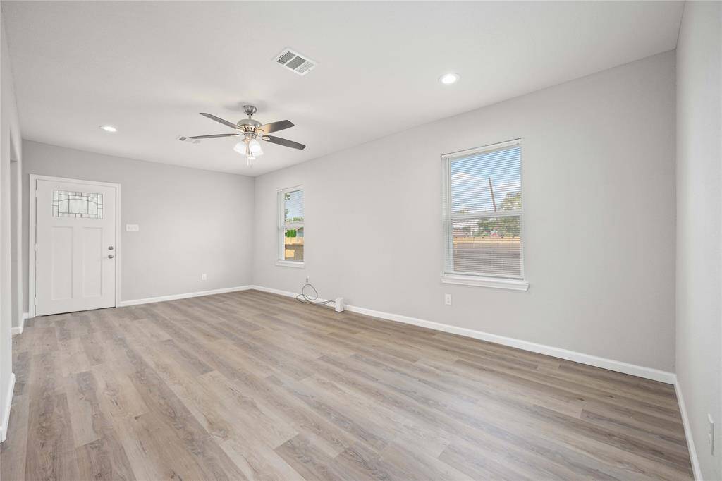 Bright, spacious living area with modern laminate flooring, ceiling fan, and neutral walls. Features ample natural light from large windows and a stylish front door. Perfect for comfortable living and entertaining.
