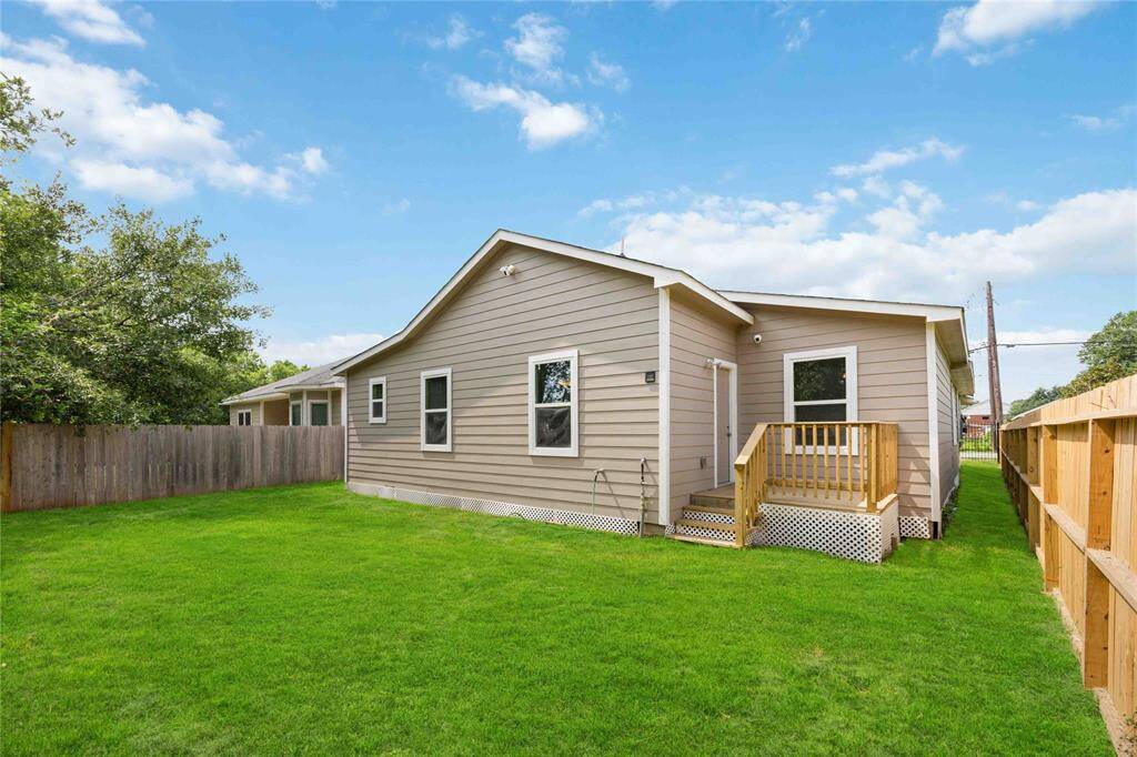 This photo showcases a charming single-story home with a well-maintained backyard. It features a small wooden deck, light siding, and a fenced yard, perfect for outdoor activities.