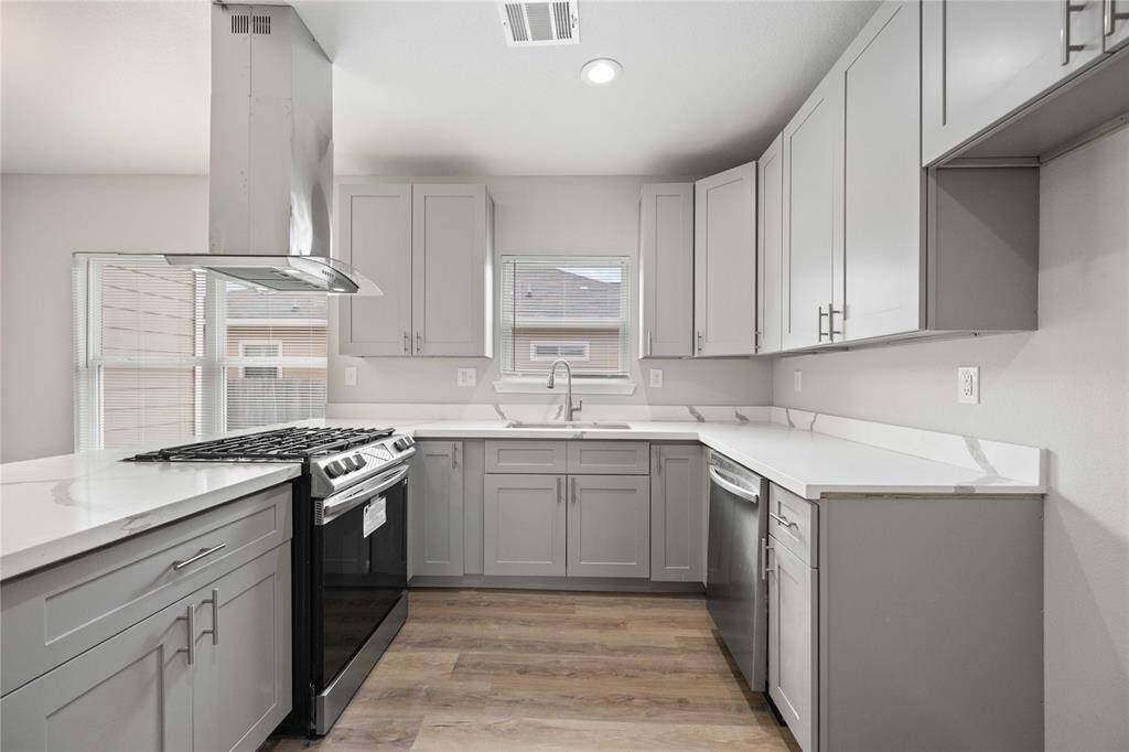 Modern kitchen with sleek gray cabinets, stainless steel appliances, and a central gas stove. The room features ample natural light and fresh white countertops, creating an inviting and functional space.