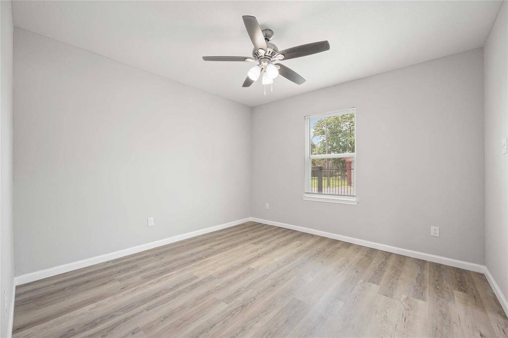 This room features modern gray walls and wood-style flooring, complemented by a ceiling fan. A large window provides natural light, creating a bright and inviting space.