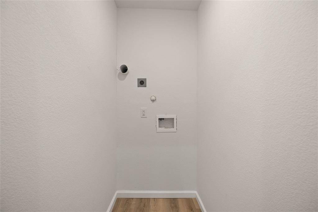 This photo shows a laundry area with hookups for a washer and dryer, featuring neutral walls and hardwood flooring.