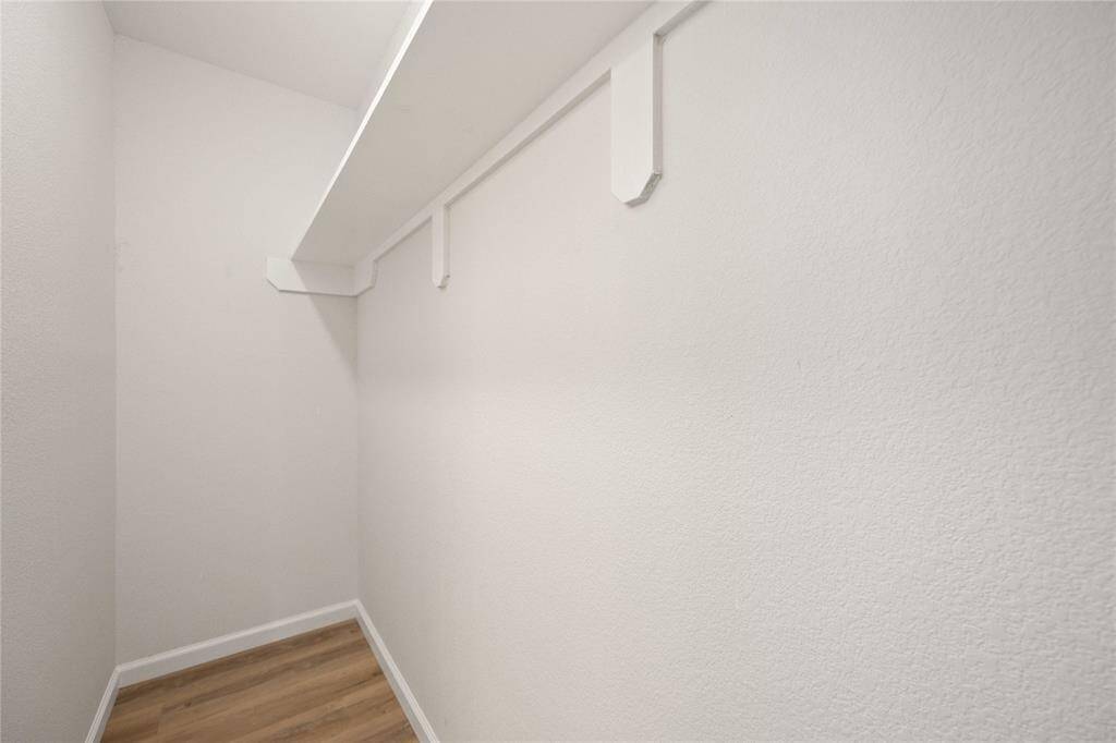 This photo shows a small walk-in closet with white walls and wood flooring. It features a single shelf and hanging rail, ideal for organizing clothes and accessories.