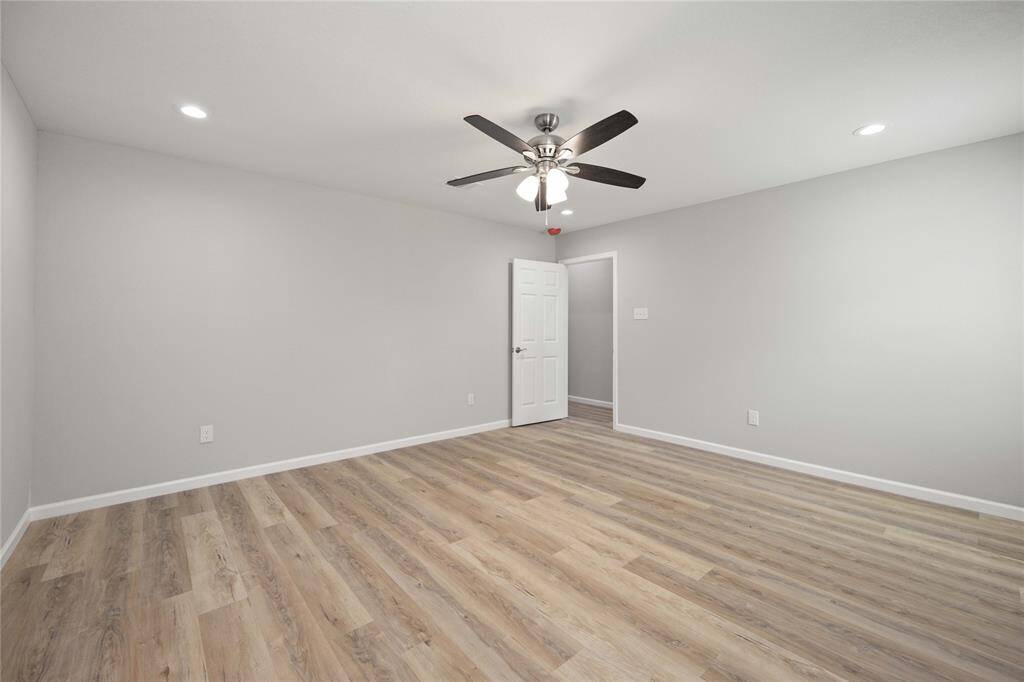 This spacious room features light gray walls, wood-look flooring, and recessed lighting. A ceiling fan adds comfort, and the room is bright and modern with clean lines.