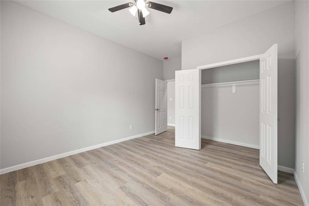 This bright, neutral-toned bedroom features laminate wood flooring, a ceiling fan, and a spacious open closet, offering a clean and modern look.