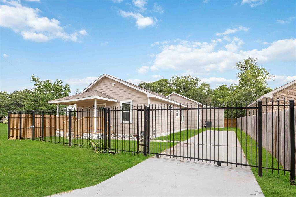 This photo shows a charming single-story home with a fenced yard and driveway. The exterior features a gable roof and neutral siding, set against a backdrop of lush greenery.