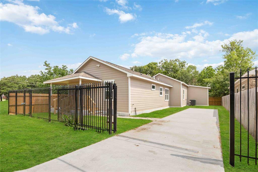 Charming single-story home with a spacious driveway and fenced yard. It features a covered front porch, modern siding, and is surrounded by lush greenery, offering privacy and a cozy atmosphere.