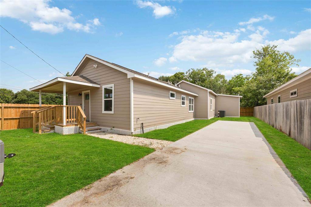 This photo shows a charming, single-story home with a beige exterior, a small porch, and a spacious driveway. The property is fenced, offering a green lawn and a cozy, private setting.