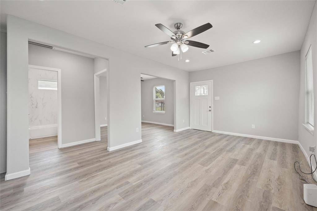 Bright, open living space with light wood floors, neutral walls, and recessed lighting. Features a ceiling fan, lots of natural light, and easy access to adjacent rooms.