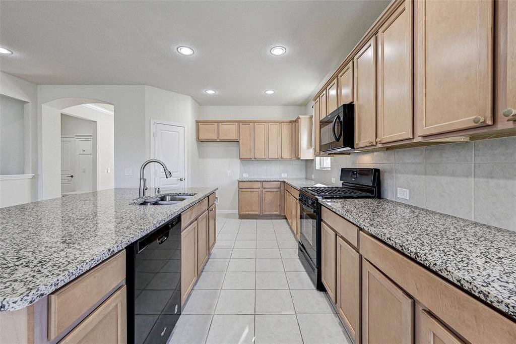 This kitchen features a spacious layout with granite countertops, ample wooden cabinetry, and modern appliances. It includes a large island with a sink, tile flooring, and plenty of natural light from multiple windows. Perfect for cooking and entertaining.