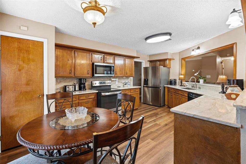 This kitchen features warm wooden cabinetry, stainless steel appliances, and a spacious layout with a cozy breakfast area. The countertops are sleek, and the lighting provides a welcoming ambiance, making it ideal for both cooking and entertaining.