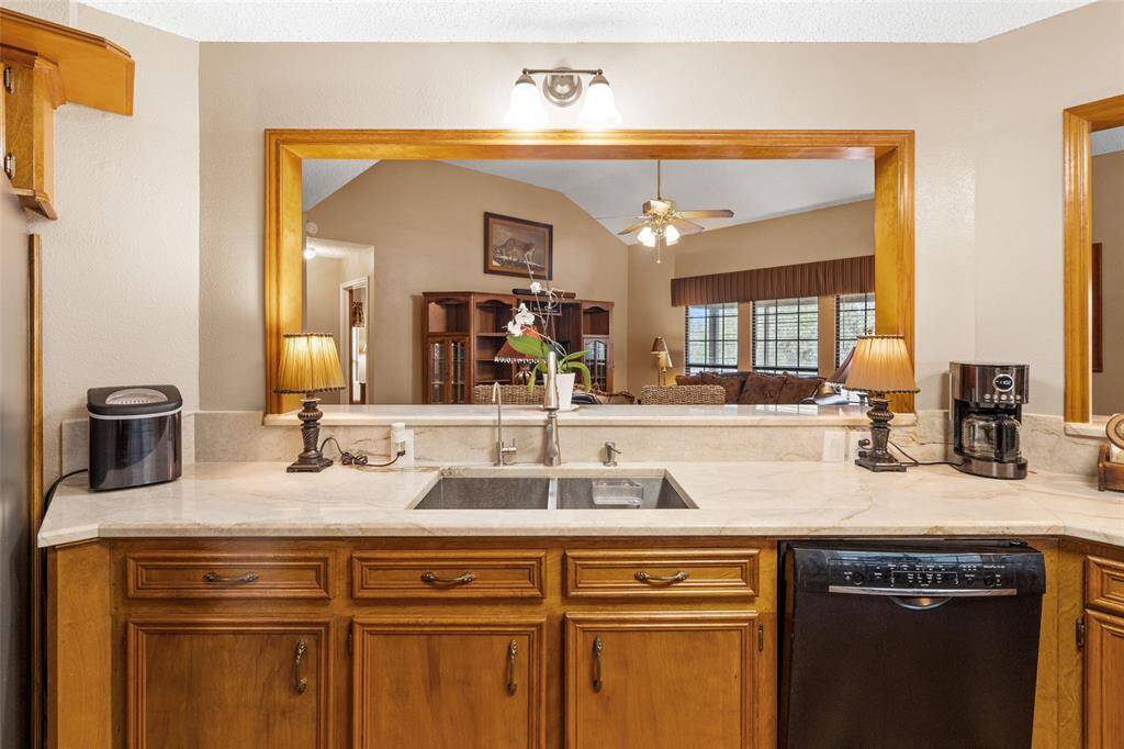 This kitchen features a spacious counter with a double sink, wooden cabinetry, and modern appliances. A large pass-through window connects to the living area, enhancing the open feel.