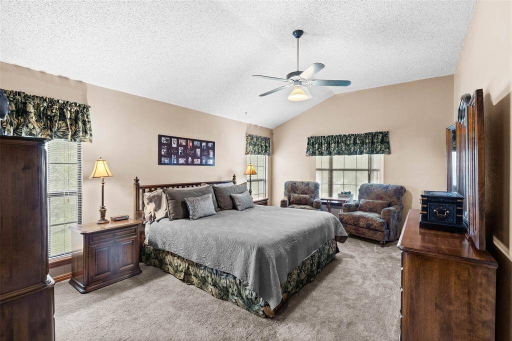 Spacious primary bedroom features vaulted ceilings, neutral walls, and cozy carpet and a space for a sitting area.