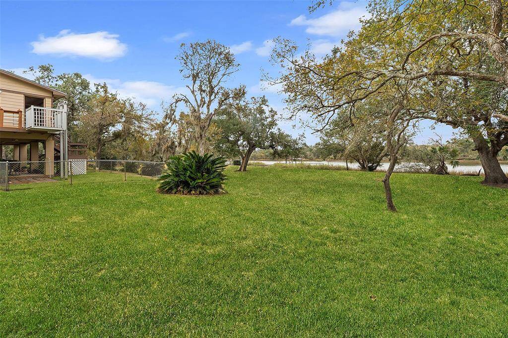 Spacious backyard with lush green grass and mature trees, offering a serene view. The home features a balcony and a fenced area, ideal for enjoying outdoor activities.