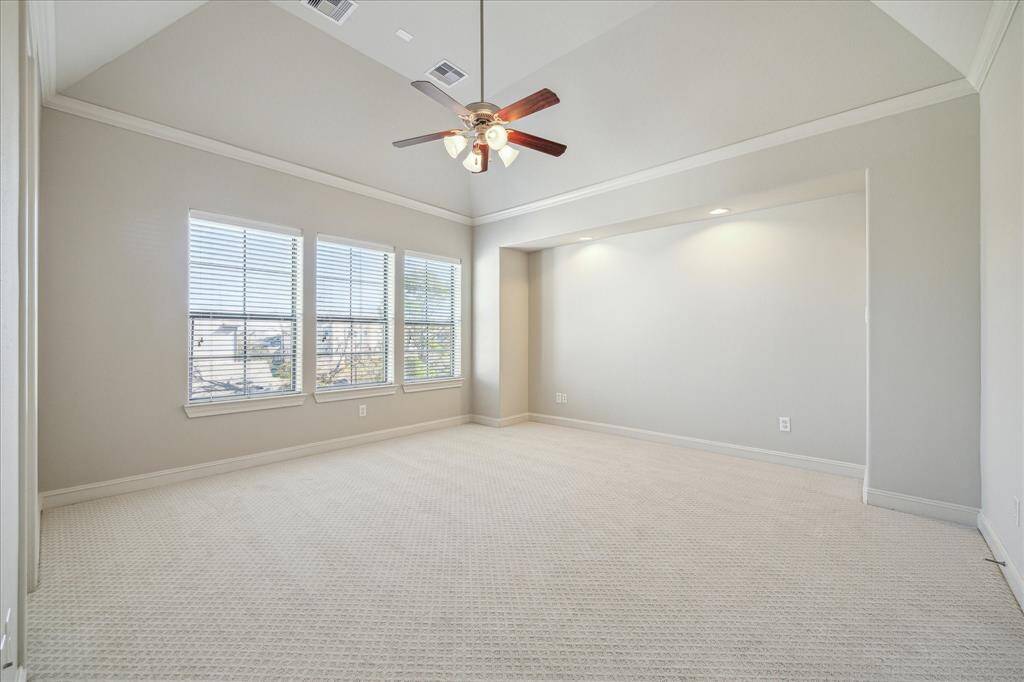 This spacious bedroom features neutral walls, a vaulted ceiling with a ceiling fan, and large windows for natural light. Recessed lighting adds a modern touch, and the carpeted floor ensures a cozy atmosphere.