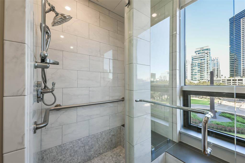 The standup shower in the primary bathroom with seamless glass door and marble surround.