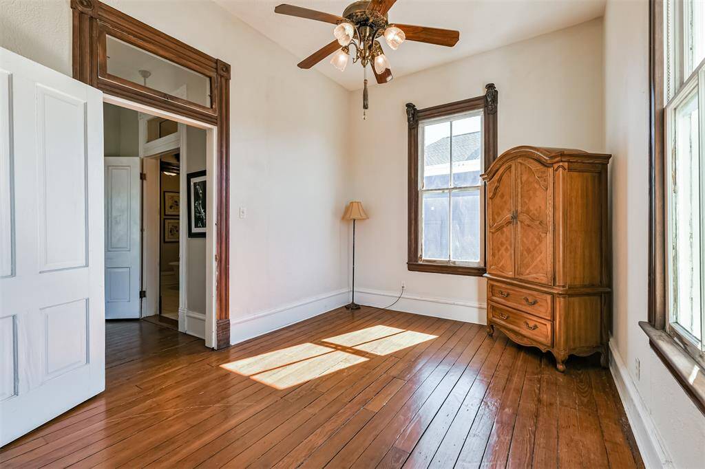 Another secondary bedroom is adjacent to the previous room and just outside the door of the full bathroom. This bedroom offers a lighted ceiling fan, continued wood floors, ornately cased windows, and an original transom window above the door.