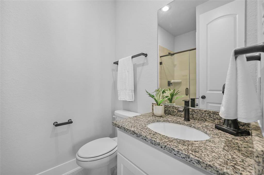 The secondary downstairs bedroom's ensuite full bath featuring granite countertops & a frameless glass shower.