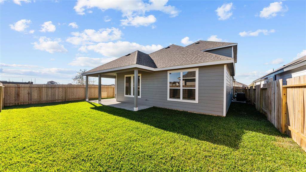 This photo showcases the backyard of a house with a covered patio, fenced yard, and well-maintained lawn. Perfect for outdoor activities and relaxation.