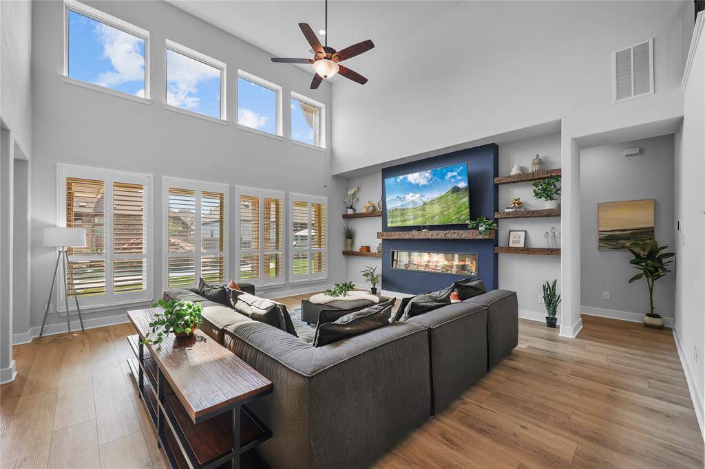 Wow! This stunning living room is the heart of the home. Two-story ceilings, picture perfect windows adorned with plantation shutters, custom faux wood shelving, a modern electric fireplace, and a grand open floorplan set the stage for luxury living.