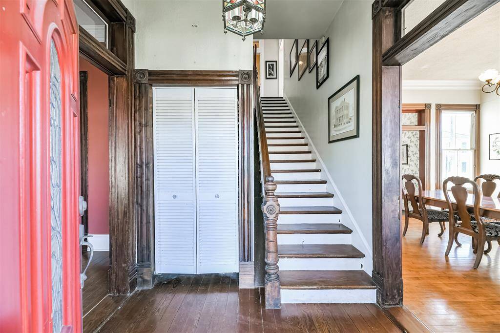 From the covered front porch, step through the solid wood door with a decorative leaded glass insert and take a step back in time into this foyer with the original hardwood floors, a stained glass light fixture, and the staircase straight ahead.
