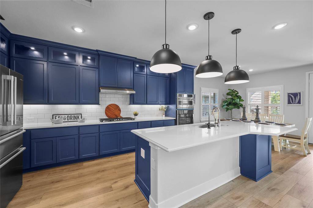 Hello from your new kitchen! The striking blue Benedettini luxury cabinetry compliments the neutral white Omegastone countertops, the backsplash, and the pristine stainless steel appliances.