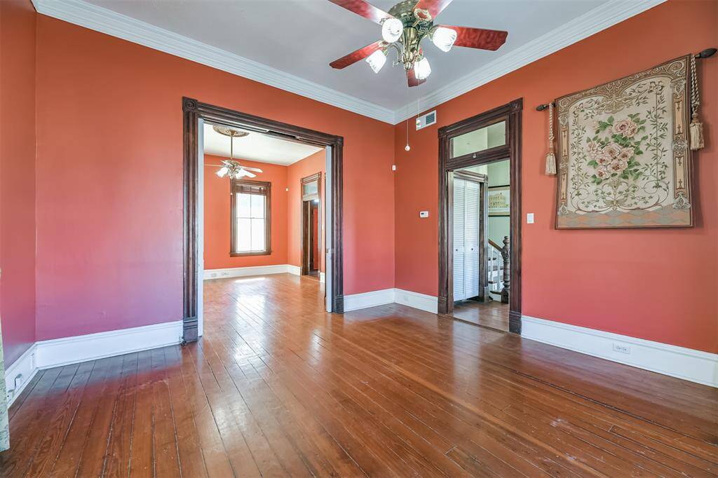 The formal living space in the home is located just inside the front door.  Notice the oversized crown molding and floorboards, beautiful original door casings, transom window, wood floors, lighted ceiling fan with a ceiling medallion, and pocket door access to the adjacent library/den.
