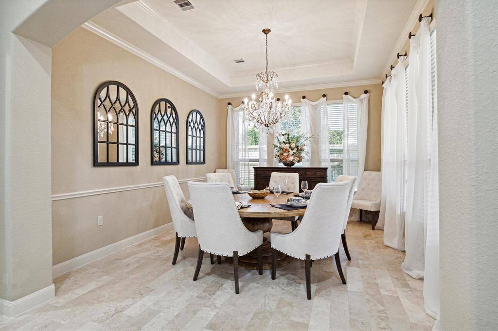 Elegant dining room with a chandelier, large windows, and continued travertine flooring throughout.