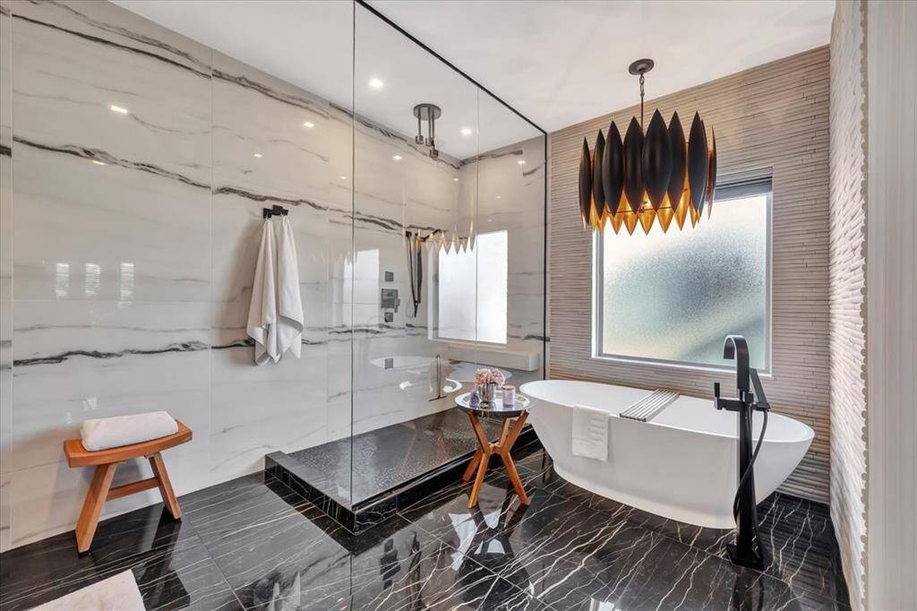The entirely remodeled primary ensuite evokes the ambiance of a luxurious hotel, featuring a spacious walk-in shower, a freestanding soaker tub, and meticulously crafted details that transform the space into a private spa retreat.